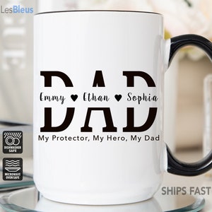 May include: White ceramic mug with a black handle. The mug has a black graphic that says "DAD" with the names "Emmy", "Ethan", and "Sophia" written below. The text "My Protector, My Hero, My Dad" is written below the names.