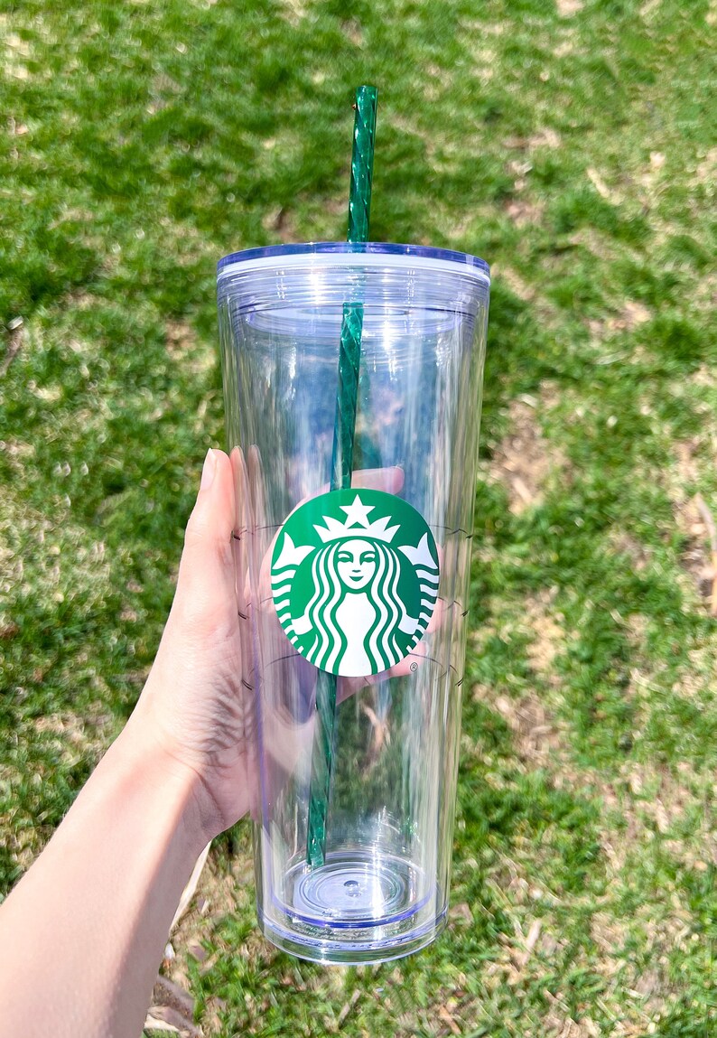 May include: A clear plastic tumbler with a green lid and a green straw. The tumbler has a Starbucks logo on the side.