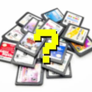 May include: A pile of video game cartridges with a yellow pixelated question mark in the foreground. The cartridges are in black cases with colorful labels. The background is white.