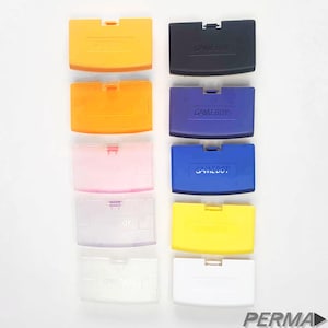 May include: Ten Game Boy Advance game cartridge cases in various colors, including orange, black, blue, pink, yellow, and white. The cases are all in the same style, with a curved top and a flat bottom. The word "GAMEBOY" is printed on the front of each case.