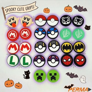 May include: A collection of circular silicone thumbstick grips featuring various character and icon designs including ghosts, red and white balls, black and white animal faces, green leaves, yellow bat symbols, red spider webs, and green pixelated faces.