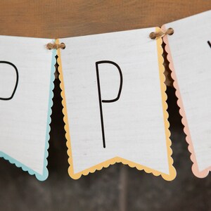 May include: A white banner with the word "HAPPY" written in black. The banner is made of paper and has a scalloped edge. Each letter is on a separate flag with a different colored border: blue, yellow, and pink.
