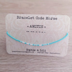 Peut inclure: Un bracelet en perles turquoise et blanches avec le mot "AMITIE" écrit en code morse. Le bracelet est présenté sur une carte avec les mots "Bracelet Code Morse" et "Sophie & Lili".