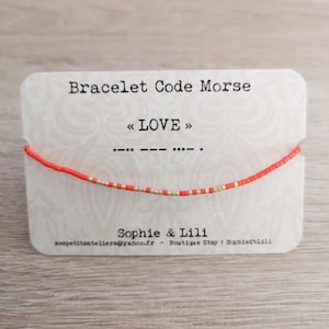 Peut inclure: Un bracelet en perles rouge et or avec le mot "LOVE" écrit en code Morse sur une carte blanche. La carte comprend également le texte "Bracelet Code Morse" et "Sophie & Lili".