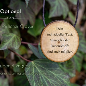Może przedstawiać: Drewniany wisiorek z czarnym sznurkiem, z tekstem "Dein individueller Text. Symbole oder Runenschrift sind auch m&ouml;glich." Wisiorek wisi na zielonej gałęzi z liśćmi.