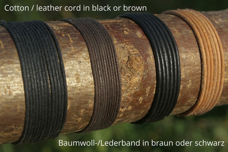 Może przedstawiać: Zbliżenie na cztery sznurki owinięte wok&oacute;ł drewnianego kloca. Sznurki są czarne, brązowe, czarne i brązowe. Tekst "Cotton / leather cord in black or brown" znajduje się w g&oacute;rnej części obrazu. Tekst "Baumwoll-/Lederband in braun oder schwarz" znajduje się w dolnej części obrazu.
