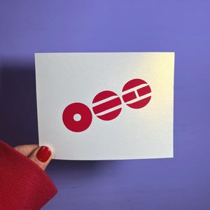 May include: A white card with a red graphic of three connected circles. The first circle is solid, while the other two have horizontal and vertical lines. The card is held against a purple background.