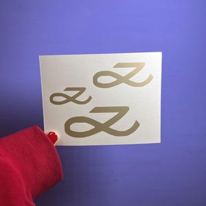 May include: A white ceramic mug with a black handle and the text "But First, Coffee" in a black, handwritten-style font. The mug is on a white surface.