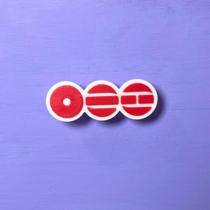 Könnte beinhalten: Ein weiß-rotes dekoratives Emblem mit drei verbundenen kreisförmigen Formen. Der erste Kreis hat einen roten Mittelpunkt, der zweite hat drei rote horizontale Linien und der dritte ein rotes H-förmiges Design. Das Emblem befindet sich auf einem lila Hintergrund.