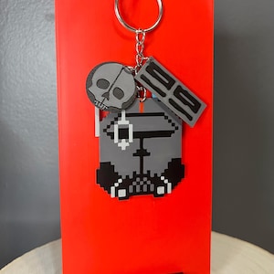 Pode incluir: Uma caneca de cerâmica branca com uma alça preta e o texto "But First, Coffee" em negrito preto. A caneca está sobre um fundo neutro, destacando seu design simples.