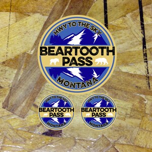 May include: Three round stickers with a blue and gold design. The stickers feature a mountain range with the text "HWY TO THE SKY BEARTOOTH PASS MONTANA".