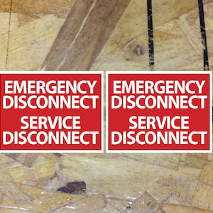 May include: Two red signs with white text on a wood background. The signs read "Emergency Disconnect Service Disconnect".