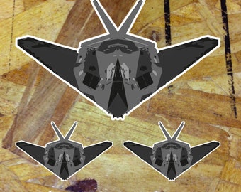 May include: Three gray paper cutouts of a stealth fighter jet on a woodgrain background.