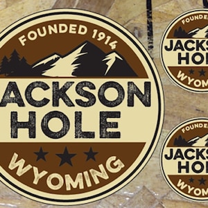 May include: Three brown and beige circular stickers with the text "FOUNDED 1914 JACKSON HOLE WYOMING" and a mountain silhouette.
