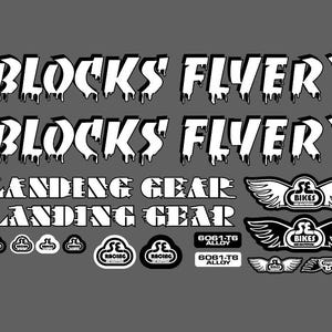 May include: A collection of white and black bicycle decals. The text includes "BLOCKS FLYER", "LANDING GEAR", "SE BIKES", "6061-T6 ALLOY", and "SE RACING". The decals feature wing and cloud designs.