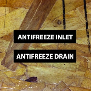 May include: Close-up of a wooden surface with black labels that read "ANTIFREEZE INLET" and "ANTIFREEZE DRAIN".