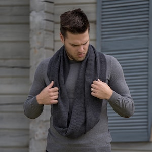 以下が含まれることがあります： グレーの長袖シャツにダークグレーのインフィニティスカーフを巻いた男性。