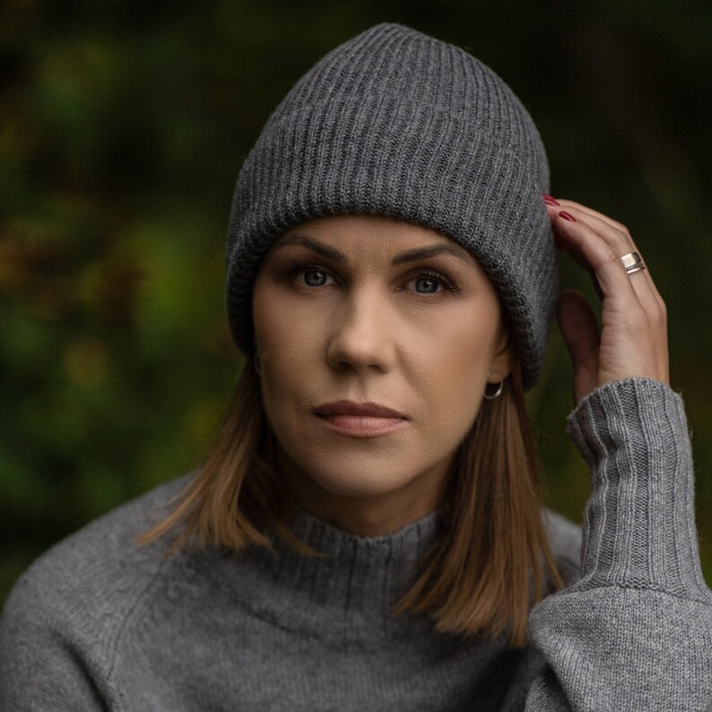 May include: A woman wearing a gray knitted beanie and a gray sweater. She is looking at the camera with a serious expression.