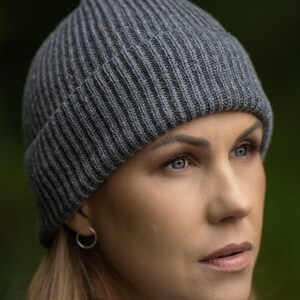 May include: A woman wearing a gray knitted beanie hat. The hat is ribbed and has a simple design.