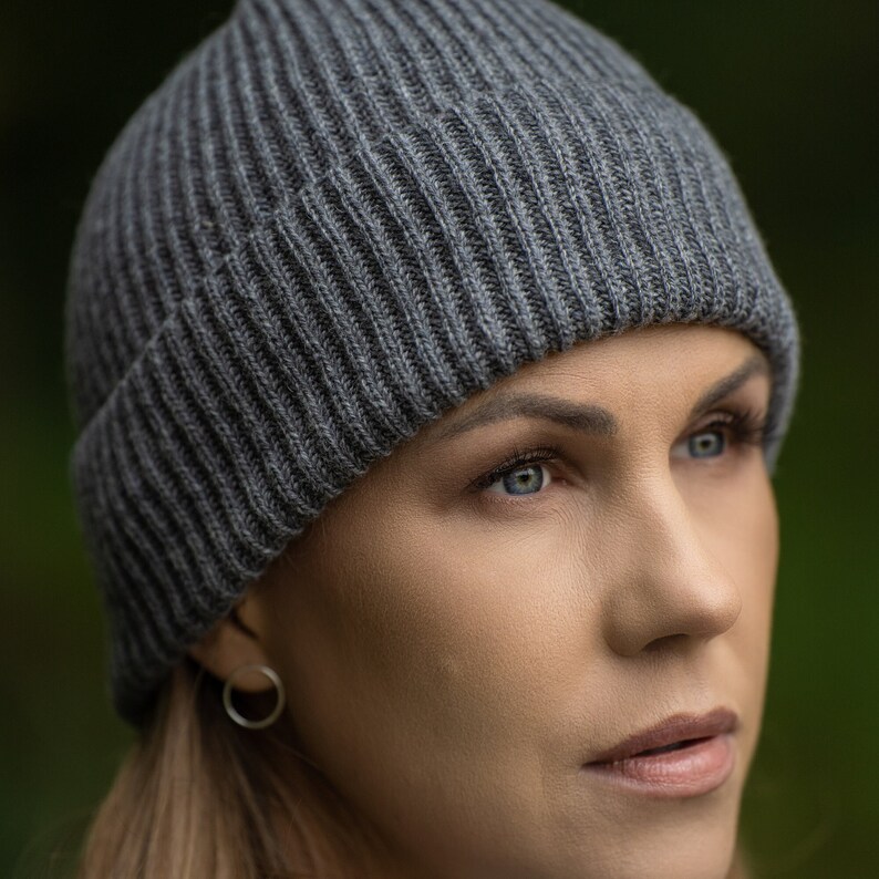 May include: A woman wearing a gray knitted beanie hat. The hat is ribbed and has a simple design.