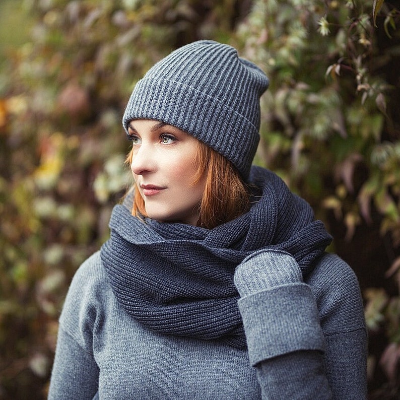 May include: A woman wearing a gray knitted hat and a matching gray scarf. The hat is a beanie style and the scarf is a long, thin scarf that is wrapped around her neck.