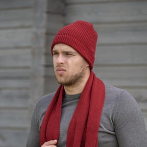 May include: A man wearing a red knitted beanie and a matching red scarf. The scarf is folded and worn around the neck. He is wearing a gray long-sleeved shirt.