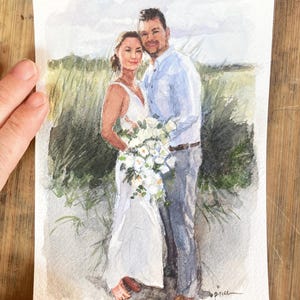 May include: Watercolor painting of a couple embracing, set against a backdrop of tall grass and a cloudy sky. The woman wears a white dress and holds a bouquet. The man is in a light blue shirt and gray pants. The artwork is signed.