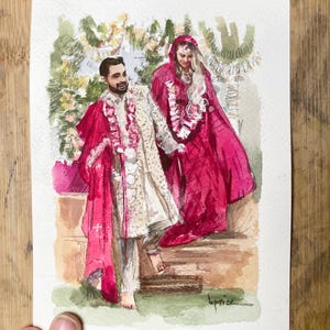 May include: Watercolor painting of a couple in traditional Indian wedding attire. The man wears a cream-colored outfit with a red shawl, and the woman is in a red sari. The artwork is on paper, with a wooden background.