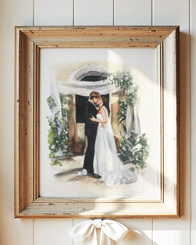 May include: Watercolor painting of a couple embracing, framed in a rustic wooden frame. The artwork depicts a bride in a white gown and a groom in a black suit, surrounded by greenery. A white bow hangs below the frame.