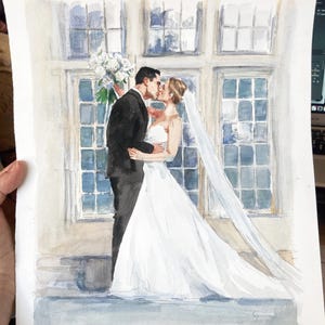 May include: Watercolor painting of a wedding couple kissing. The bride wears a white wedding dress and veil, and the groom is in a black tuxedo. A bouquet of white flowers is held by the groom. The background features large windows.