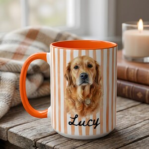 Op de afbeelding: Een keramische mok met een feloranje handvat en binnenkant, voorzien van een verticaal gestreept patroon in wit en oranje. De voorzijde toont een realistisch portret van een golden retriever met een zilveren penning en de naam Lucy eronder.