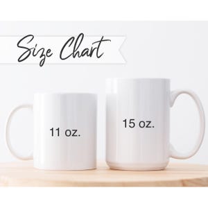 Op de afbeelding: Twee witte keramische mokken naast elkaar voor een maatvergelijking. De kleinere mok is gelabeld met 11 oz. en de grotere mok met 15 oz. Boven de mokken staat een witte banner met de zwarte tekst Size Chart in een cursief lettertype.