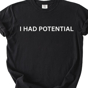 May include: A black short-sleeved t-shirt featuring the white text I HAD POTENTIAL printed in a clean, sans-serif font across the chest. The garment has a classic crew neckline and a standard fit, with a visible brand label inside the collar.
