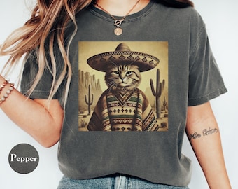 May include: A gray t-shirt with a graphic of a cat wearing a sombrero and a poncho in a desert landscape. The cat is looking directly at the viewer.