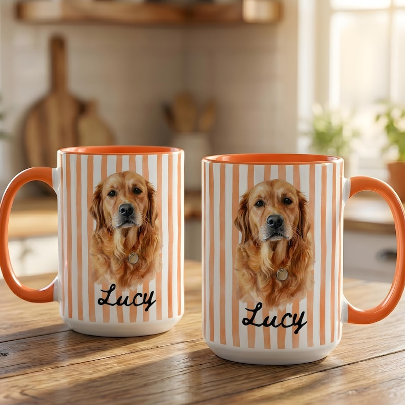 Op de afbeelding: Twee keramische mokken met een verticaal oranje en wit gestreept patroon. Elke mok toont een portret van een golden retriever en de naam Lucy in zwart cursief schrift. De mokken hebben een oranje handvat en een oranje binnenkant.