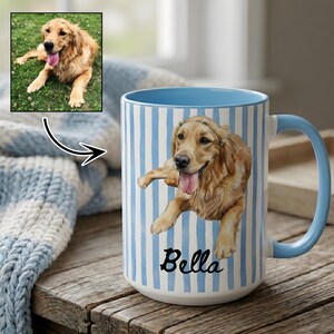 Op de afbeelding: Een keramische mok met een verticaal gestreept patroon in lichtblauw en wit. De mok toont een gedrukte illustratie van een golden retriever met de tong uit de bek, boven de naam Bella in een zwart cursief lettertype.