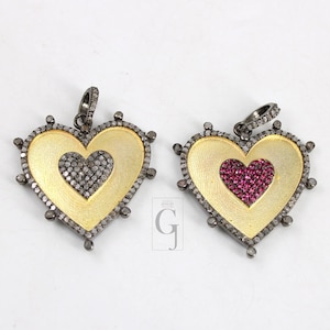 May include: Two silver heart-shaped pendants with gold accents. One pendant has a smaller heart-shaped design filled with small diamonds, while the other has a smaller heart-shaped design filled with small red gemstones.