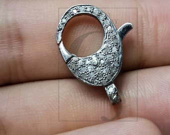 May include: A silver-colored jewelry clasp with a curved design. The clasp is encrusted with small, clear gemstones. The clasp is open and ready to be attached to a necklace or bracelet.