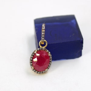 Peut inclure: Un pendentif en forme de pierre précieuse rouge avec un halo de diamants. Le pendentif est en or et possède une bélière pour l'attacher à une chaîne.