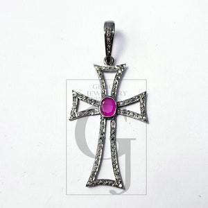 Peut inclure: Pendentif en forme de croix argentée avec une pierre précieuse rose ovale au centre. La croix est ornée de petits diamants transparents et possède un bélière décorative. Le pendentif est présenté sur une surface blanche.