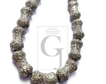 May include: A strand of silver-toned beads with a textured surface. The beads are shaped like small cylinders with a slight hourglass shape. The beads are strung on a clear thread.