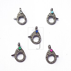 May include: Five silver-toned teardrop-shaped clasps with small, round gemstones in various colors: blue, green, pink, and turquoise. Each clasp is encrusted with small, clear gemstones around the teardrop opening.
