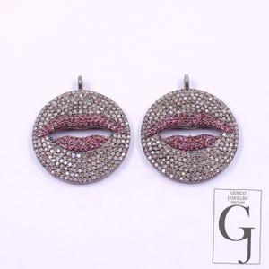 May include: Two round pendants with a silver-colored surface, each featuring a red lips design. The lips are made of small, closely set red stones. The pendants have a small loop at the top for hanging.