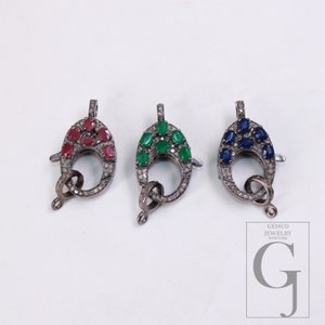 Peut inclure: Trois fermoirs de bijoux ovales avec des pierres précieuses rouges, vertes et bleues. Chaque fermoir est serti dans un métal foncé avec une bordure en forme de diamant. Ces fermoirs sont conçus pour la création de bijoux.