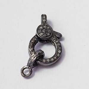 Pode incluir: Um fecho de metal preto com um anel redondo e um pequeno laço. O fecho é decorado com pequenos diamantes transparentes.