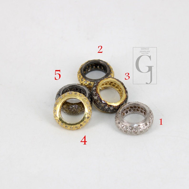 May include: Five silver and gold rings with small diamonds set in the metal. The rings are all different sizes and are arranged in a circle.