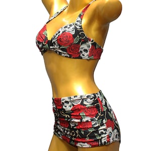 Könnte beinhalten: Ein schwarz-roter Badeanzug mit Totenkopf- und Rosenmuster. Das Oberteil ist im Halstert-Stil und das Unterteil ist ein hoch taillierter Rock.