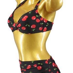 May include: A black and red cherry print bikini top and skirt. The top has a halter style with a bow in the front. The skirt is a high-waisted style with a ruched front. The bikini is made by Aloha Beachwear.