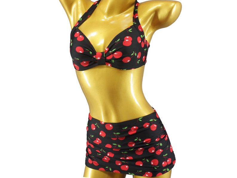 May include: A black and red cherry print bikini top and skirt. The top is a halter style with a sweetheart neckline. The skirt is a high-waisted, ruched style.