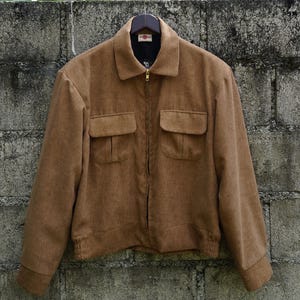 May include: A brown corduroy jacket with a zipper closure and two flap pockets. The jacket has a ribbed collar and a slightly cropped length.